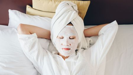 A woman with a face mask on and a towel on her head resting while on vacation. 