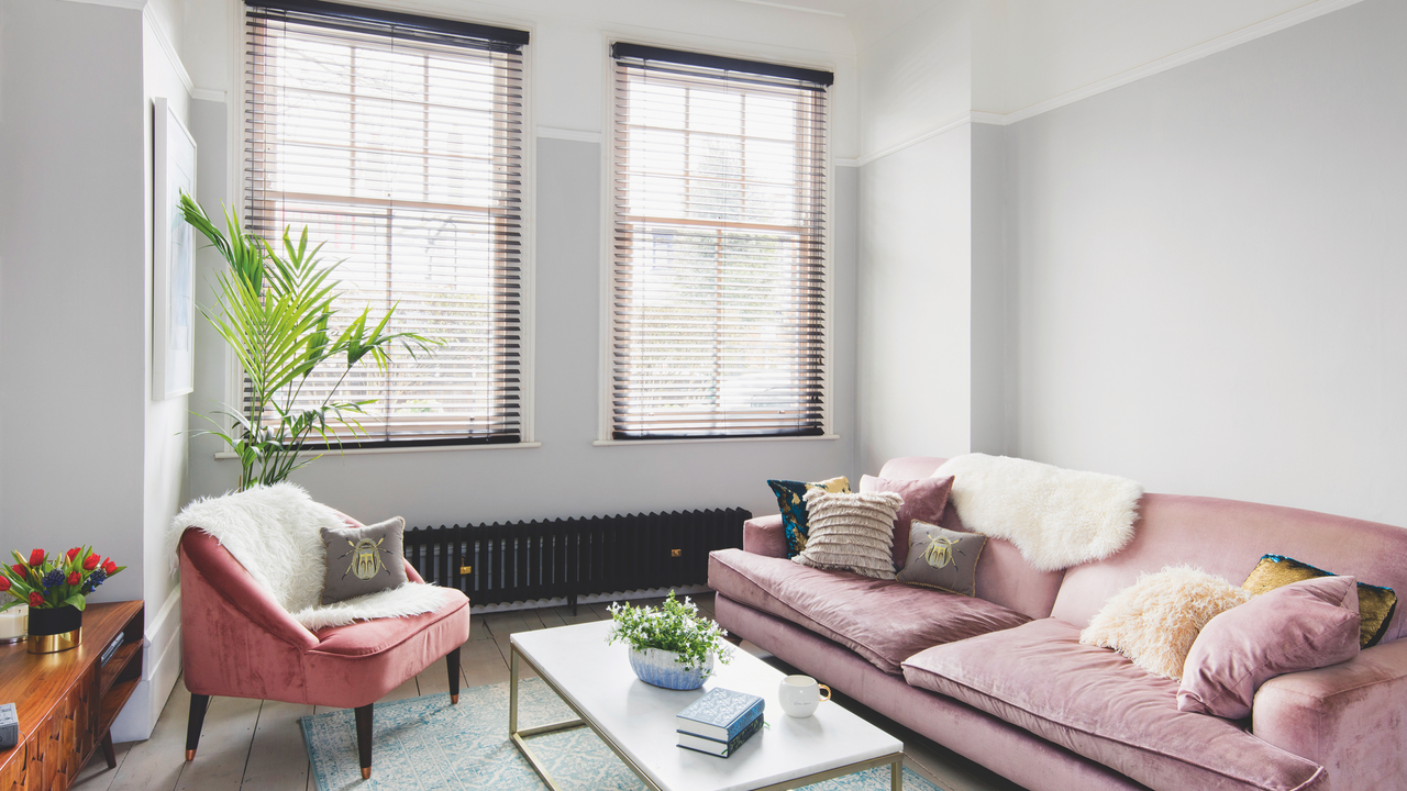 Living room with large pink sofa and armchair, pale grey painted walls and floorboards and pale blue rug. Lu and Raphael Fitoussi Findlay&#039;s small three bedroom split level flat in a Victorian House in South East London.