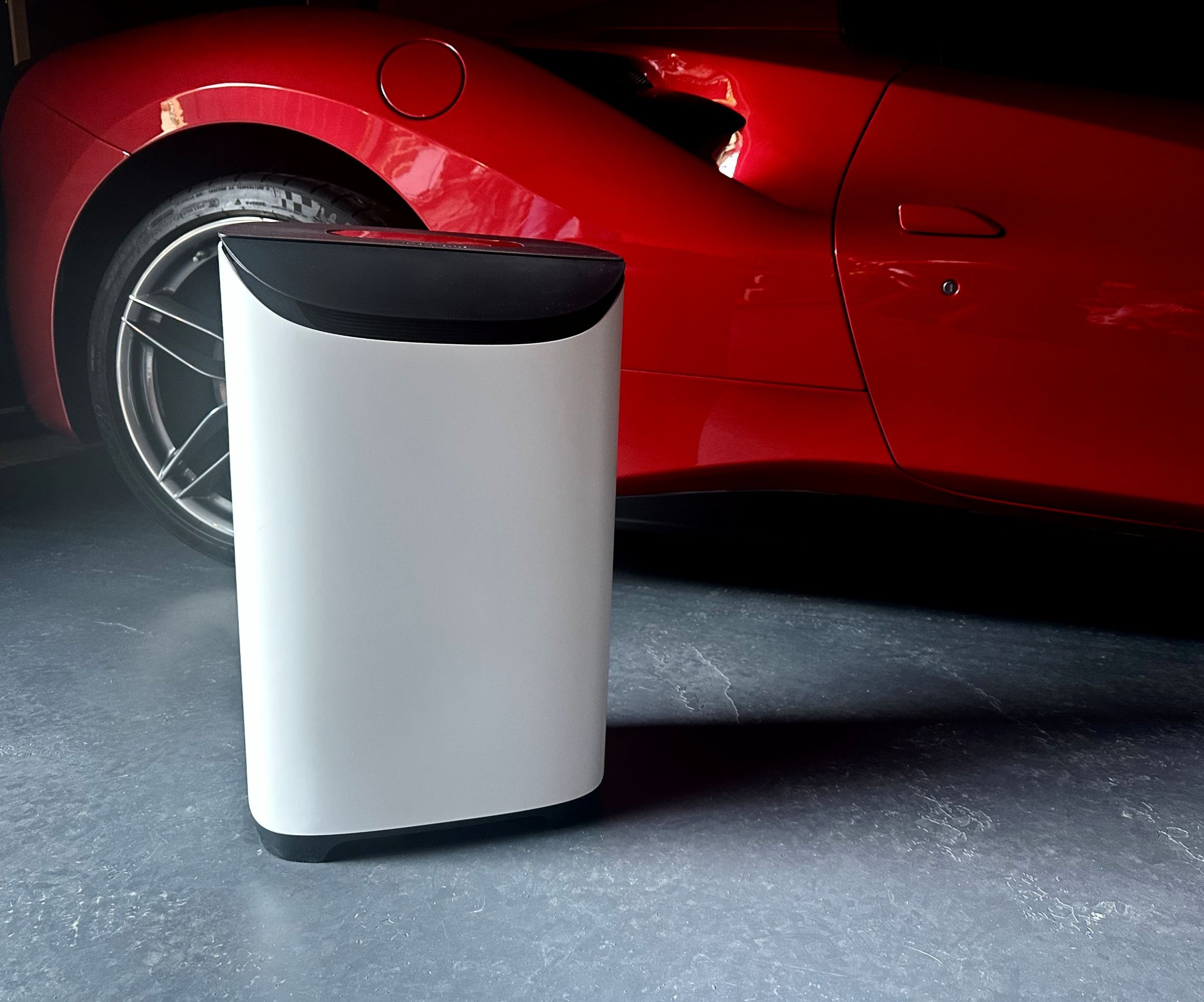 A white and black dehumidifier in front of a red super car on a concrete floor