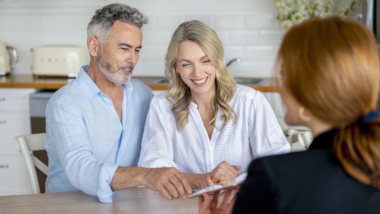 An older couple looks at a tablet held by an estate planning financial adviser. 