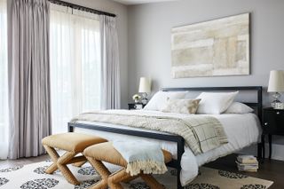 A transitional style bedroom with grey walls and a painting above the bed