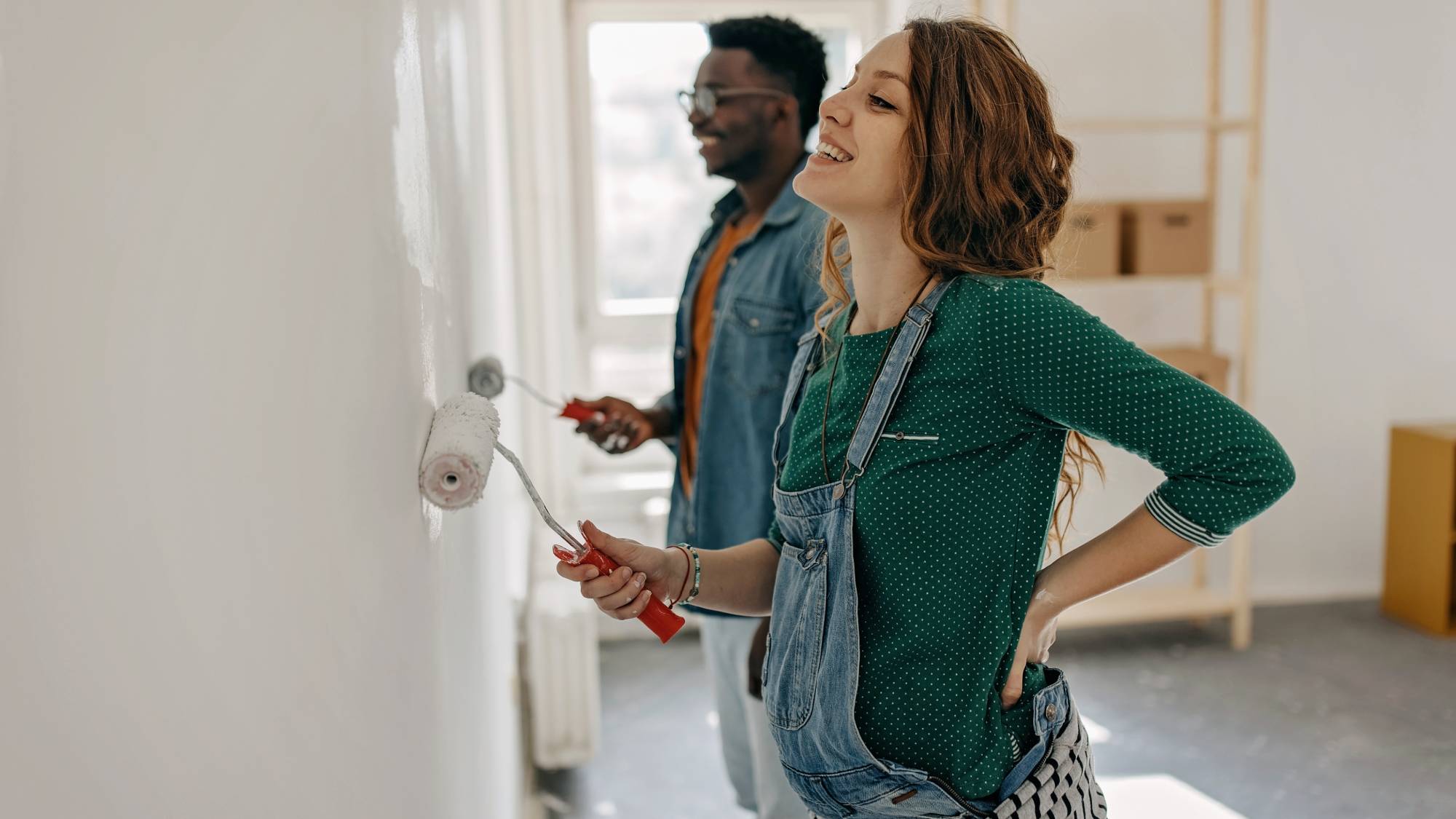 male and female painting wall with paint rollers