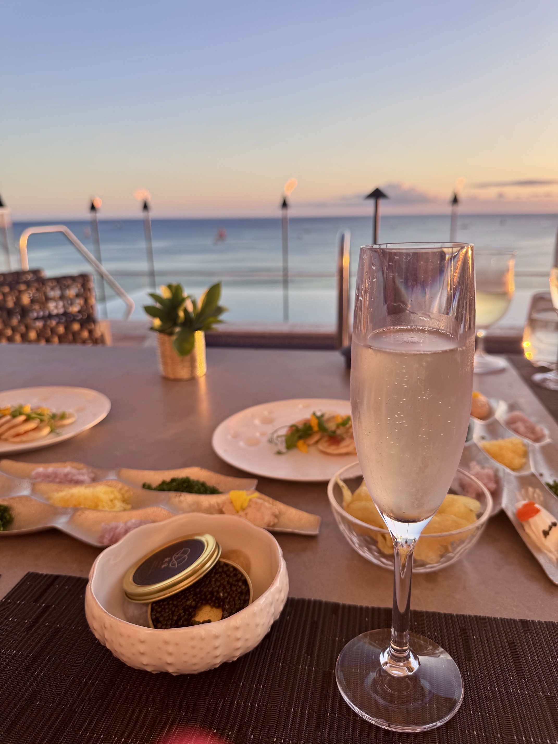A glass of champagne and plates on a table with a pool in the background
