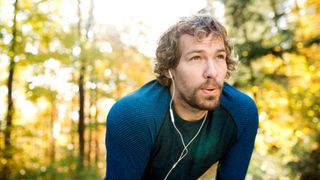 A runner wearing headphones takes a breather in the forest