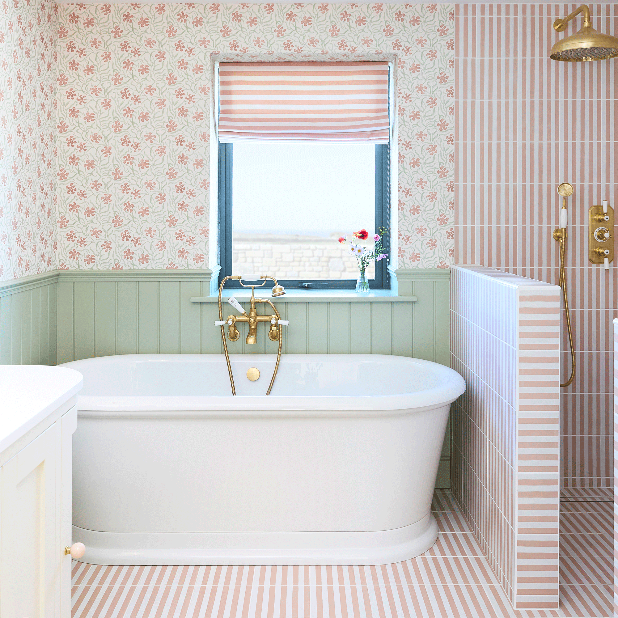 Bathroom with green wall panelling, floral wall paper, pink and white stripe tiles in shower enclosure, stripe wall lights
