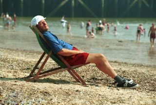 A holidaymaker with knotted hankie asleep on a sunny beach at Clacton, Essex. Image shot 2003. Exact date unknown.