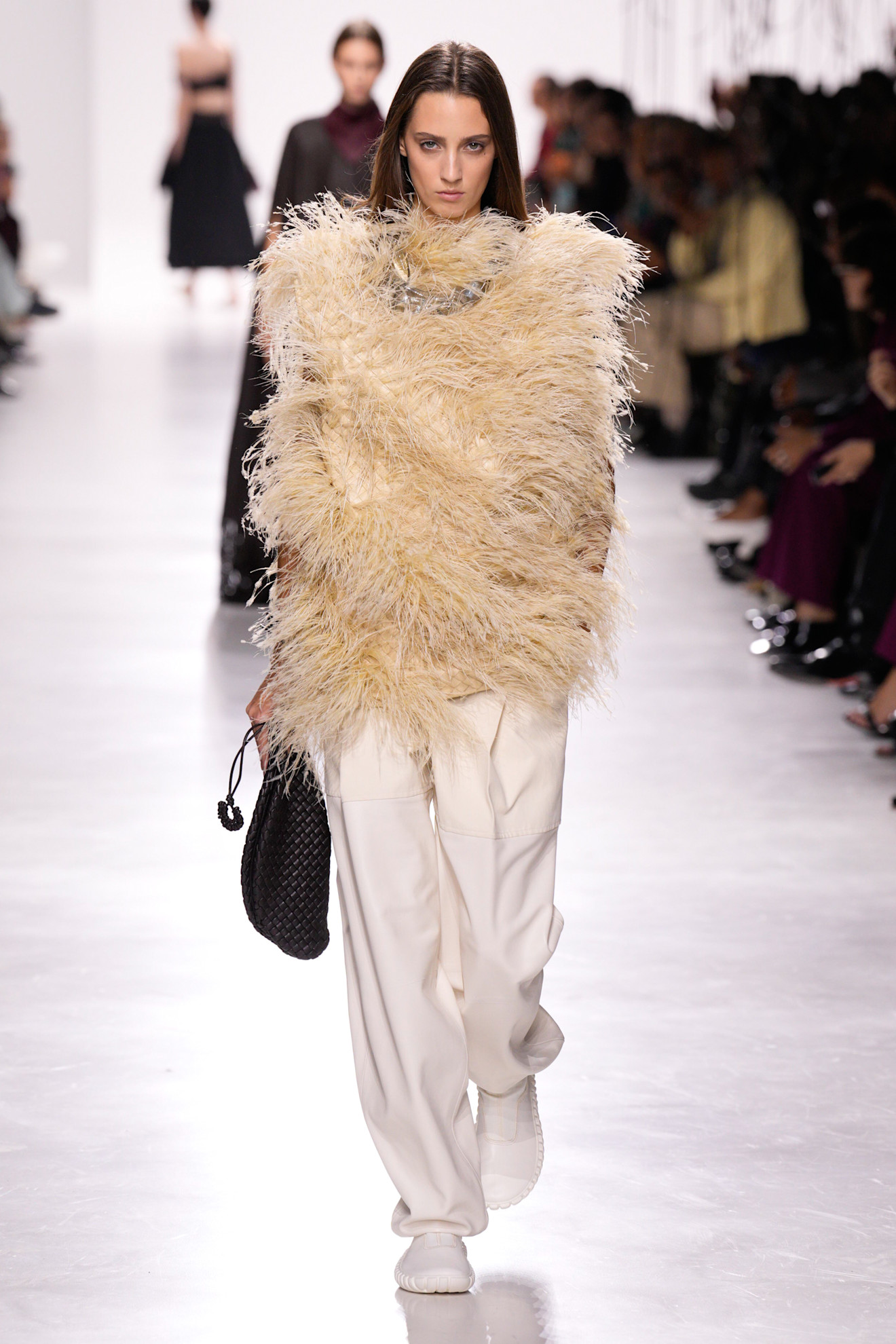 A model at the Bottega Veneta S/S 26 show wearing a feather top with classic trousers.