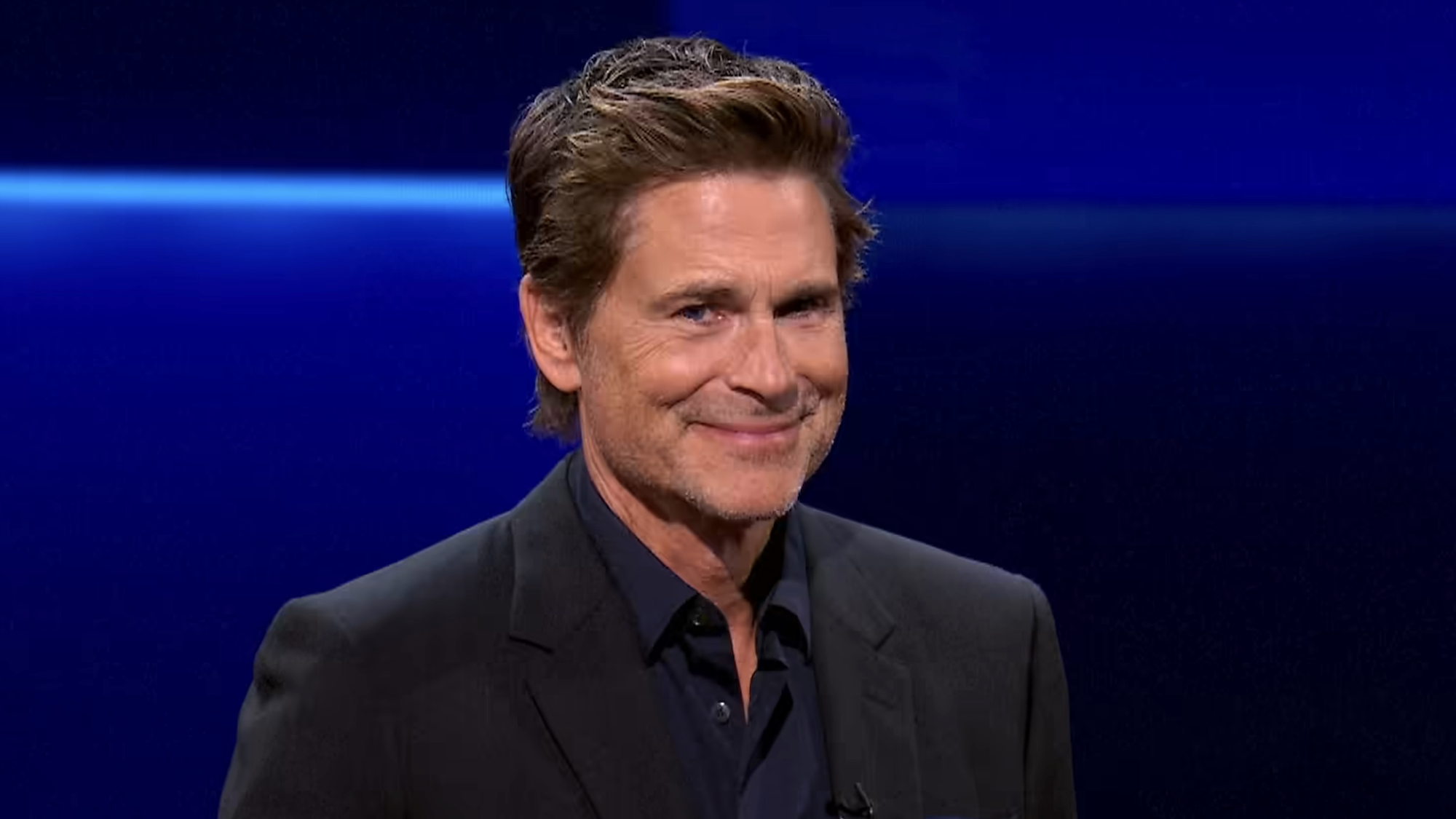 Rob Lowe smiling into camera hosting The Floor Season 6