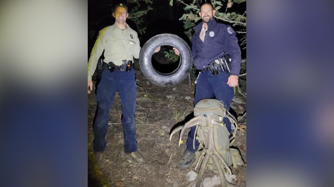 Wildlife officers Scott Murdoch (left) and Dawson Swanson (right) hold up the tire that was on this bull elk for over two years.