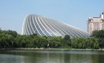 Exterior view of the curved, irregular shaped Phoenix TV building under a clear blue sky. There are trees, another building and a body of water nearby