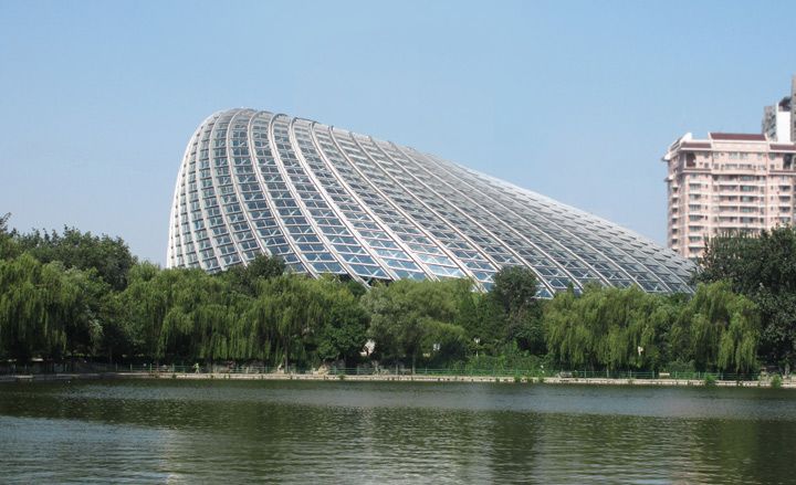 Exterior view of the curved, irregular shaped Phoenix TV building under a clear blue sky. There are trees, another building and a body of water nearby