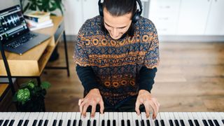 Man wearing headphones looks down at the keys of his digital piano