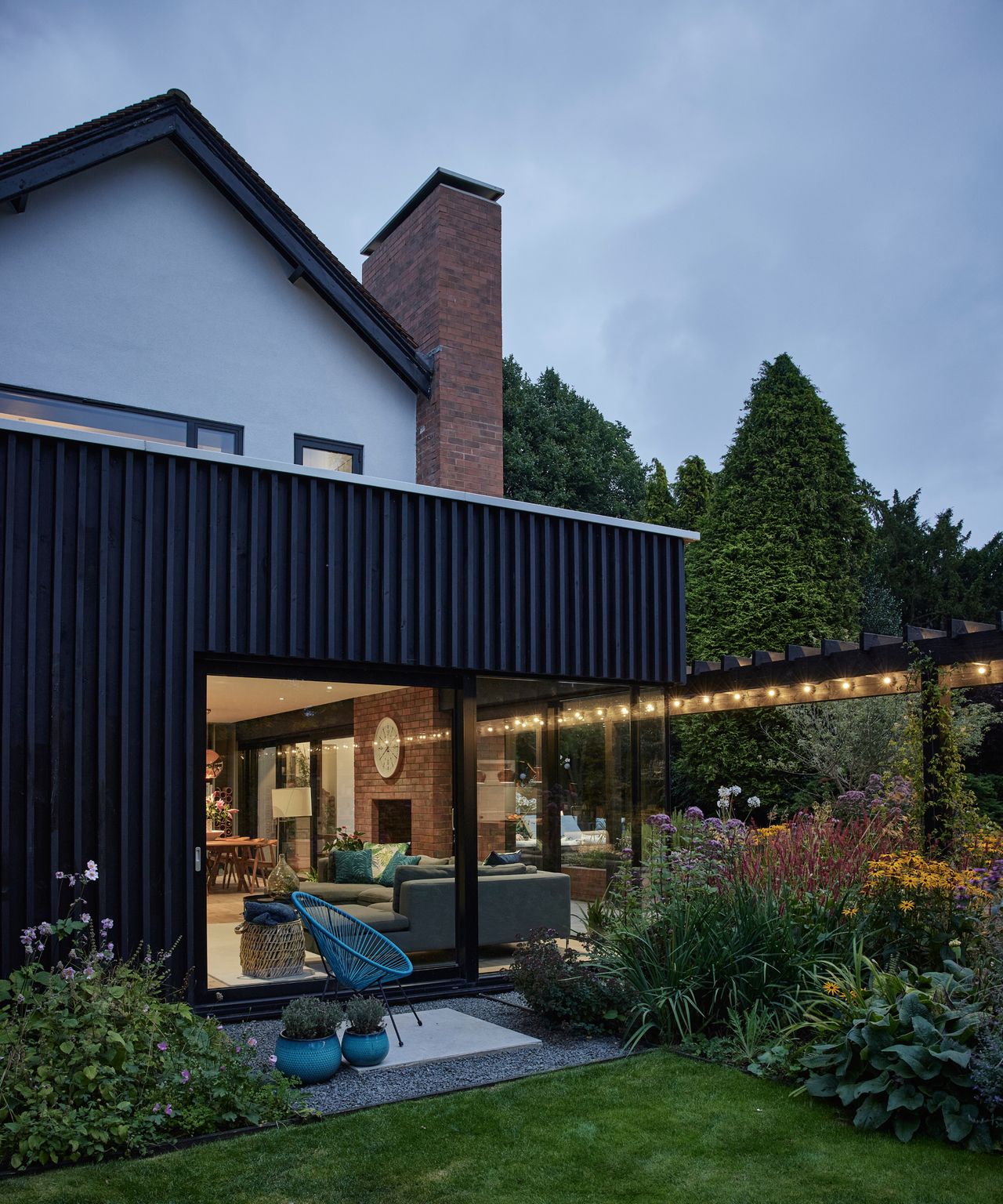 black timber clad rear extension on white rendered house with large glazed patio doors and long black pergola covered terrace