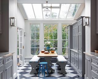 A grey kitchen extension with skylight, black and white tiled flooring and built-in storage.