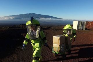 Two crew members from HI-SEAS Mission V walk uphill on the Hawaiian volcano Mauna Loa while pulling a cart of scientific equipment.