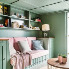 Small living room with walls, ceiling and woodwork painted sage green and a built-in sofa with pale pink cushions