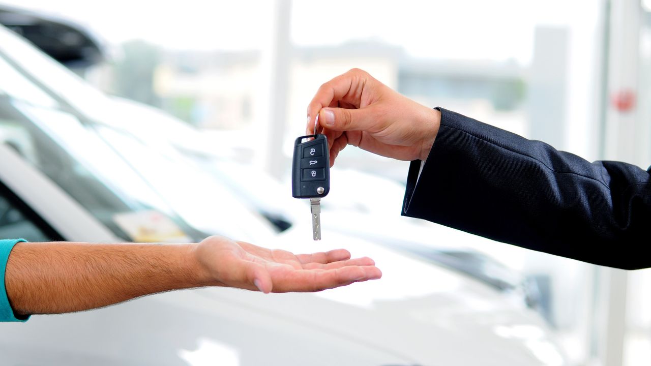 A car salesman drops a car key into the waiting hand of a buyer.