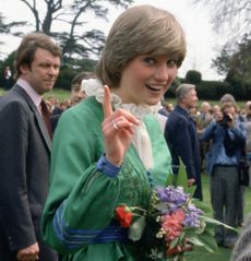 Princess Diana wearing a green dress waving her finger at the camera as a man takes a video of her