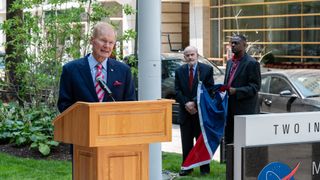 naa chief Bill Nelson stands at a podium with two people holding the juneteenth flag in the background