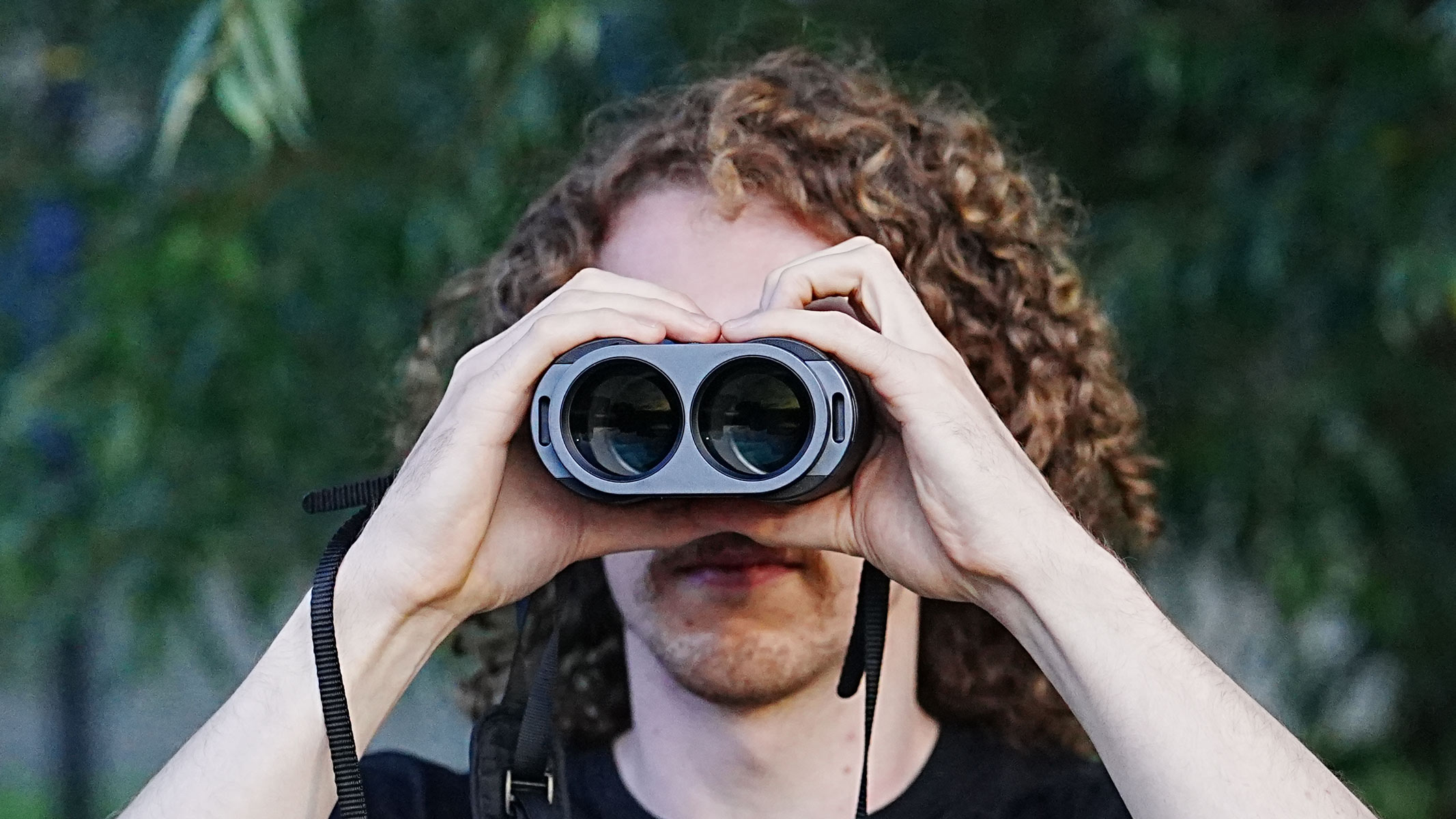A man looking forwards through the Fujifilm Techno-Stabi TS-L 1640 image-stabilized binoculars upwards with trees in the background.