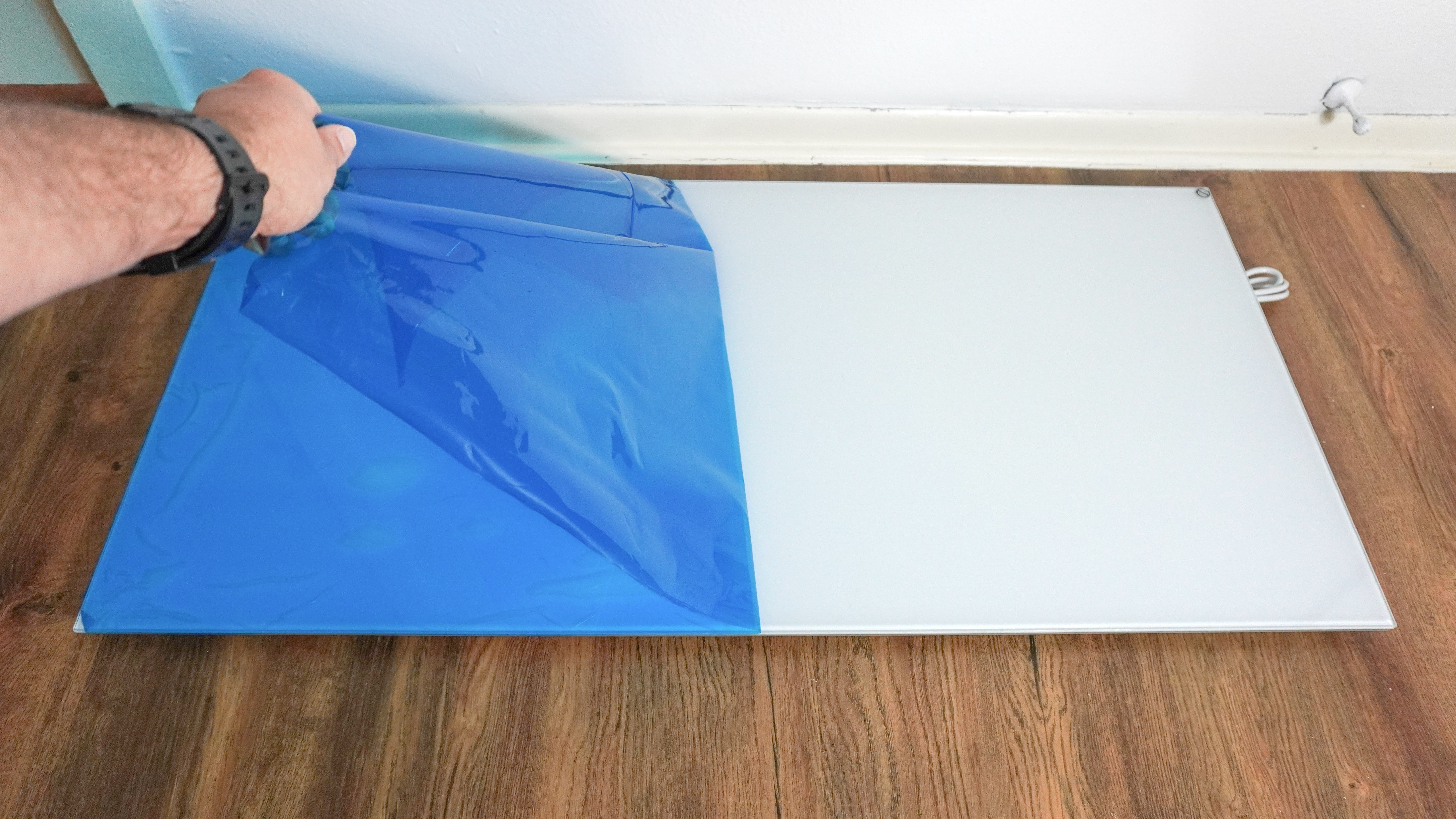 A person peeling off the protective film covering the Boldr Kelvin infrared heater to reveal its glass surface underneath