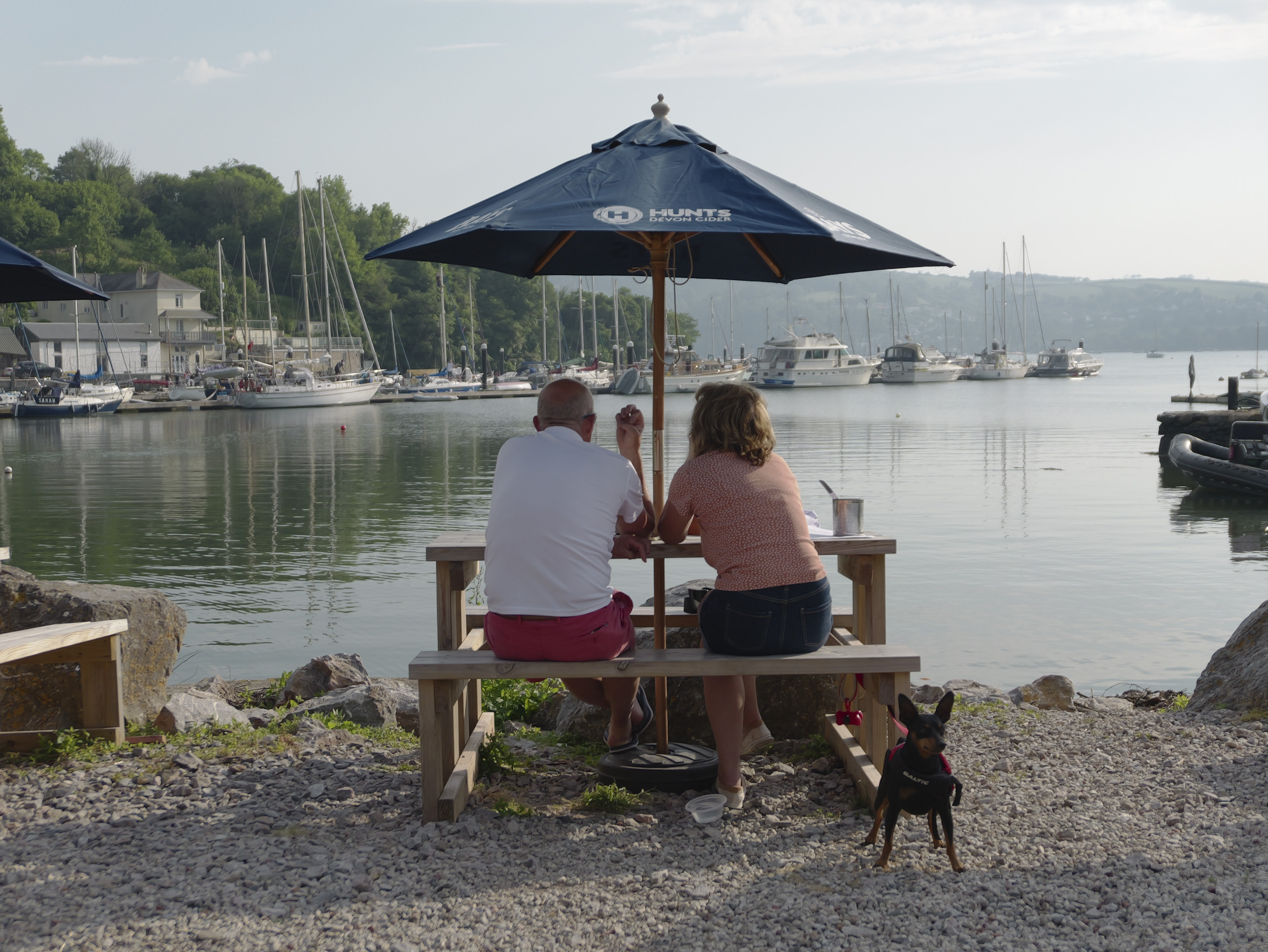 Sample image taken with the Panasonic Lumix L10; a couple sat at a bench under umbrella cover, with the tiny dog standing guard, looking out over a lake