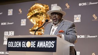 Comedian Cedric the Entertainer, dressed in dapper grey suit and off-white hat, speaks onstage ahead of the 81st Golden Globe Awards