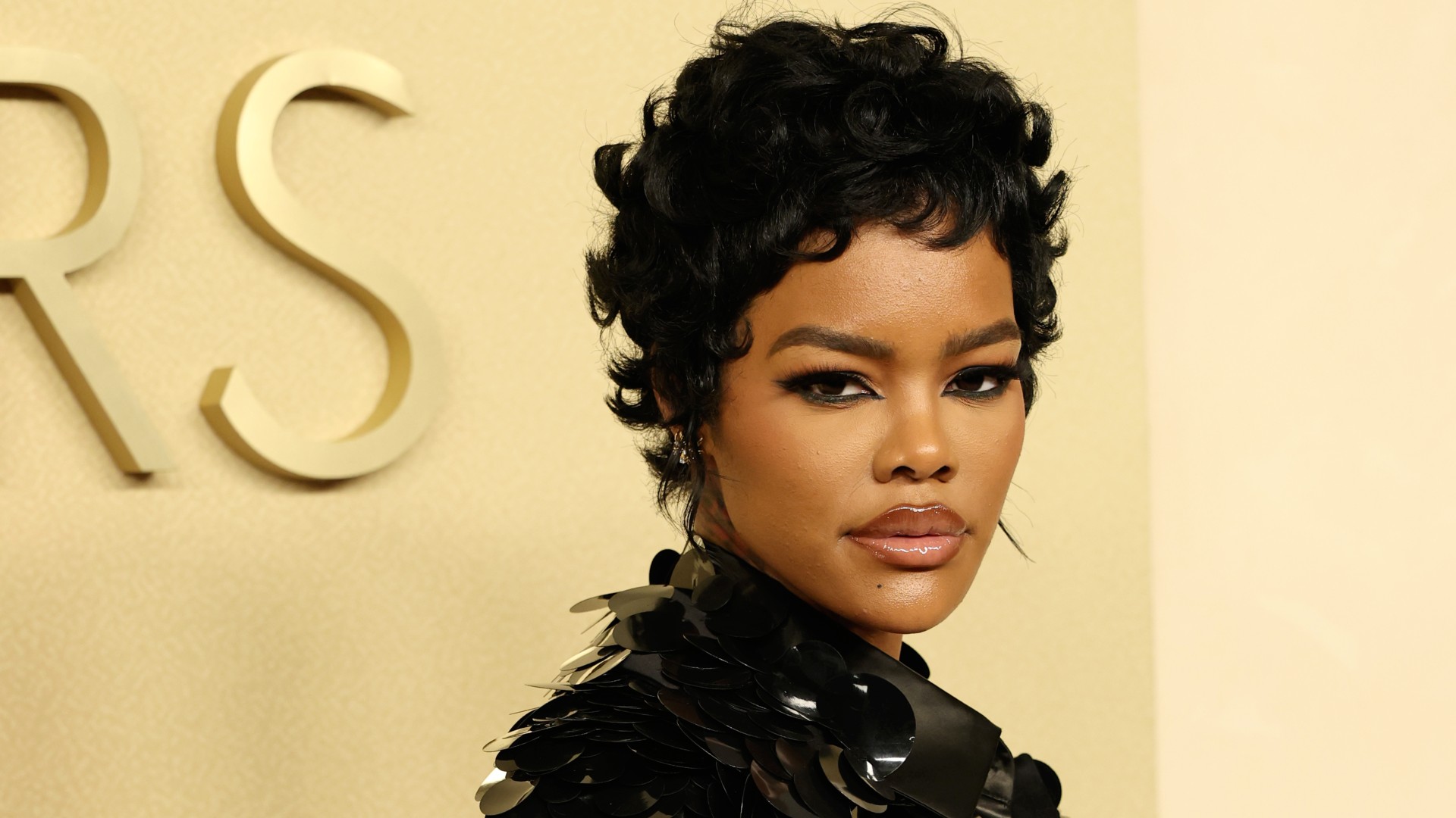 a black woman with short black hair posing on a red carpet in front of a butter yellow background