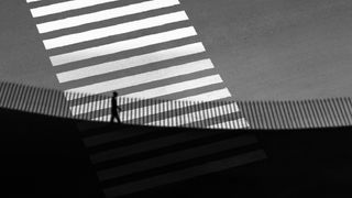 Person crossing a zebra walkway, contrasted with striped sunlight