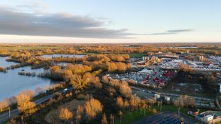 A shot from above of trees covering the centre and left of the photo, with water also featuring on the left and car parks to the right of the picture.