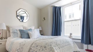 white bedroom with blue curtains open to show a sample act for how to prevent condensation on windows in bedrooms