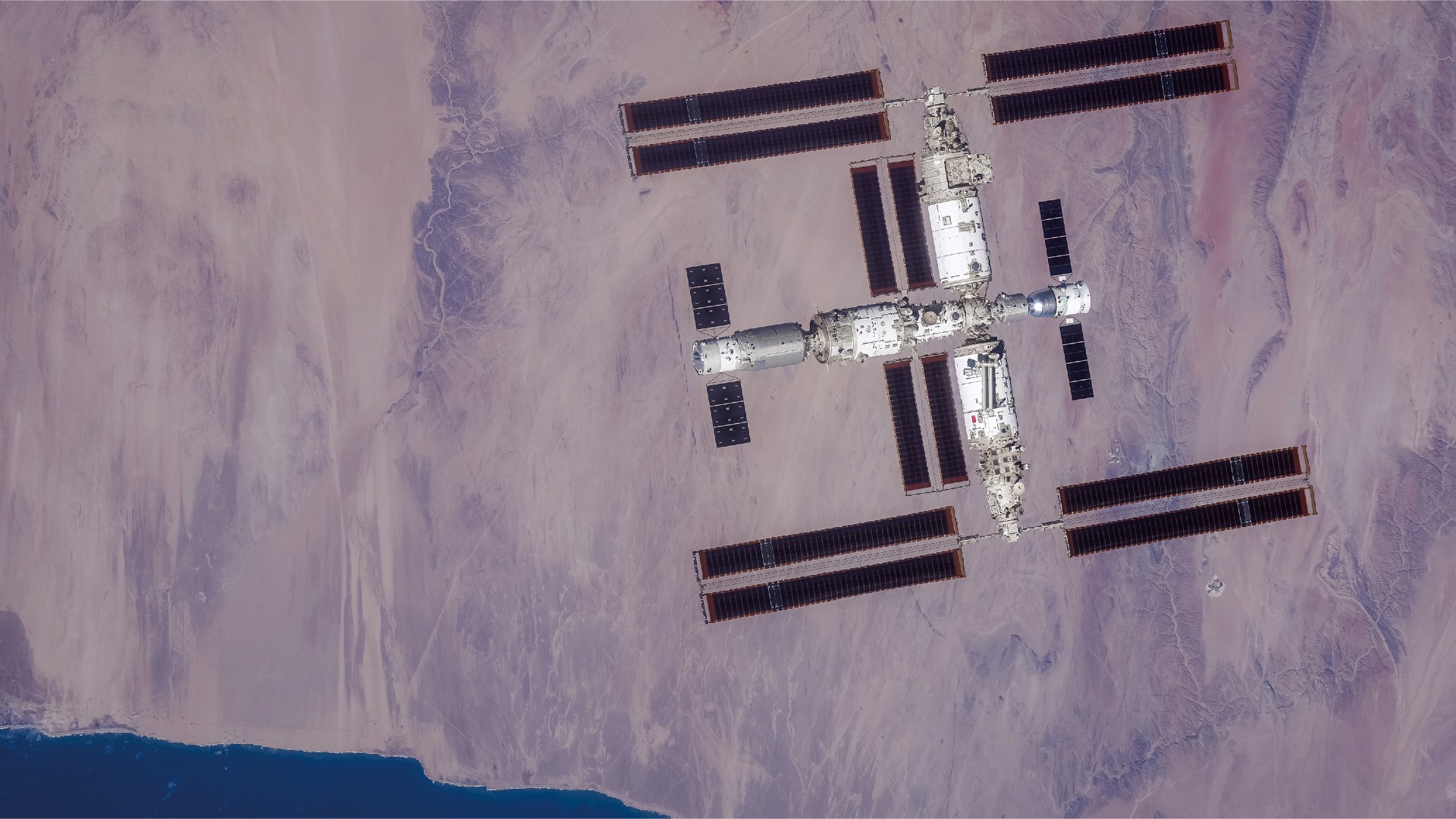 Una grande stazione spaziale a forma di T può essere vista dall'alto con la Terra sotto di essa