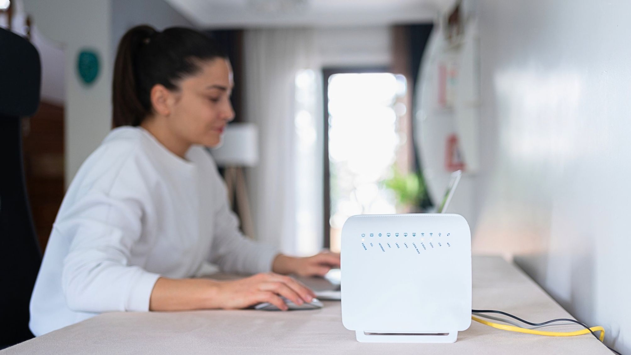A woman working on a laptop. An internet router is next to her on the right.