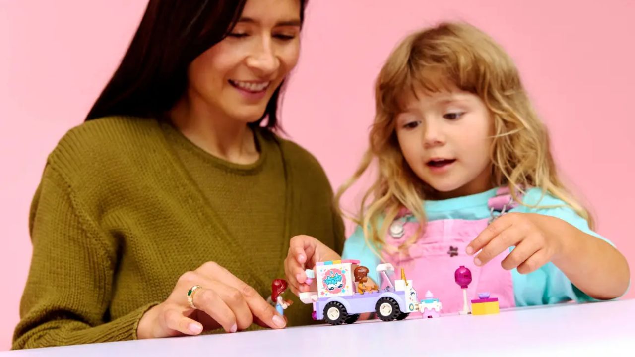 A child and adult play with a Lego set on a pink table