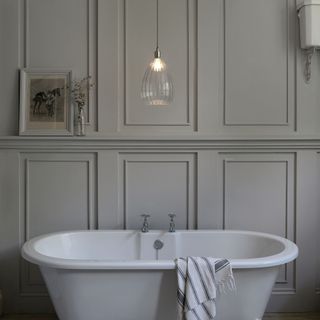 Grey panelled bathroom with classic freestanding bath and single hanging glass pendant light