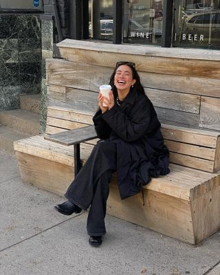 Sasha wears a black coat, black jeans, and black square-toe loafers.