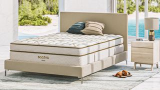 The Saatva Classic luxury innerspring hybrid mattress photographed on a cream colored faux leather bed frame
