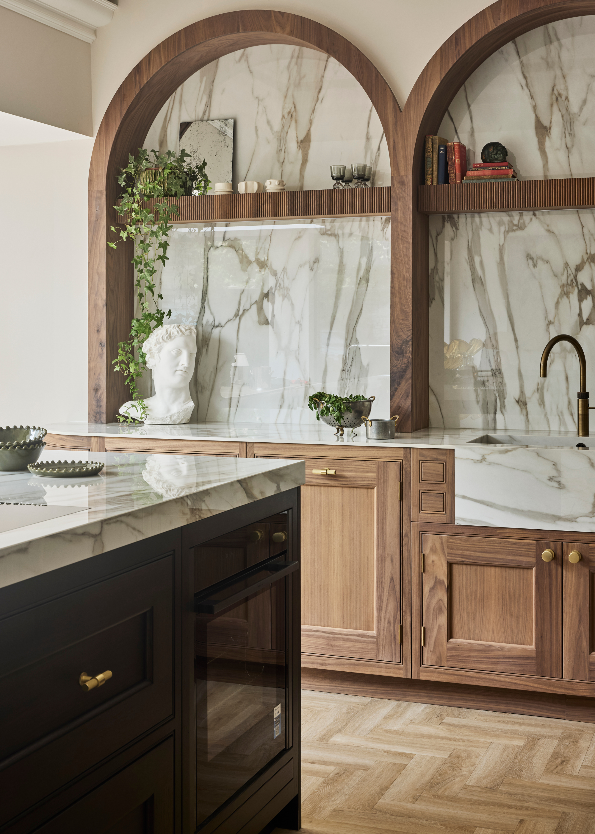 Gold handles in a kitchen with wooden cabinetry and marble counters, with a black kitchen island