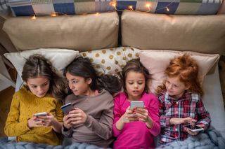 group of girls laid on bed using their phones sleepover