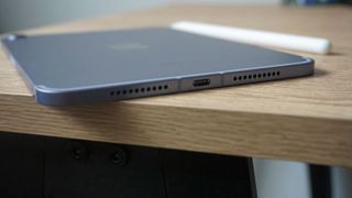 iPad mini 2021 set fra den nederste kant liggende på træoverflade med pen ved siden af