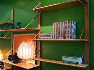 A wall with three upper wood structures and connecting shelves. Objects on the shelves include a lamp, books,.
