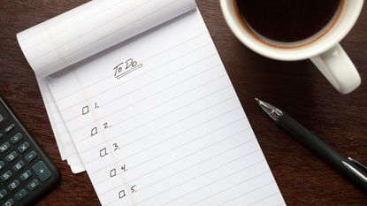 A blank to do list on a wooden desk beside a pen and a cup of coffee