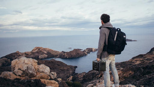 Hiker with backpack holding EcoFlow RIVER Max on rocky bluff overlooking the ocean