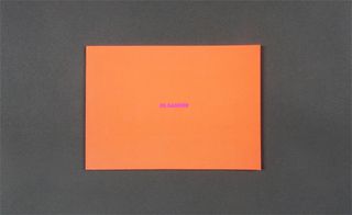 Front view of Jil Sander’s orange invitation pictured against a grey background