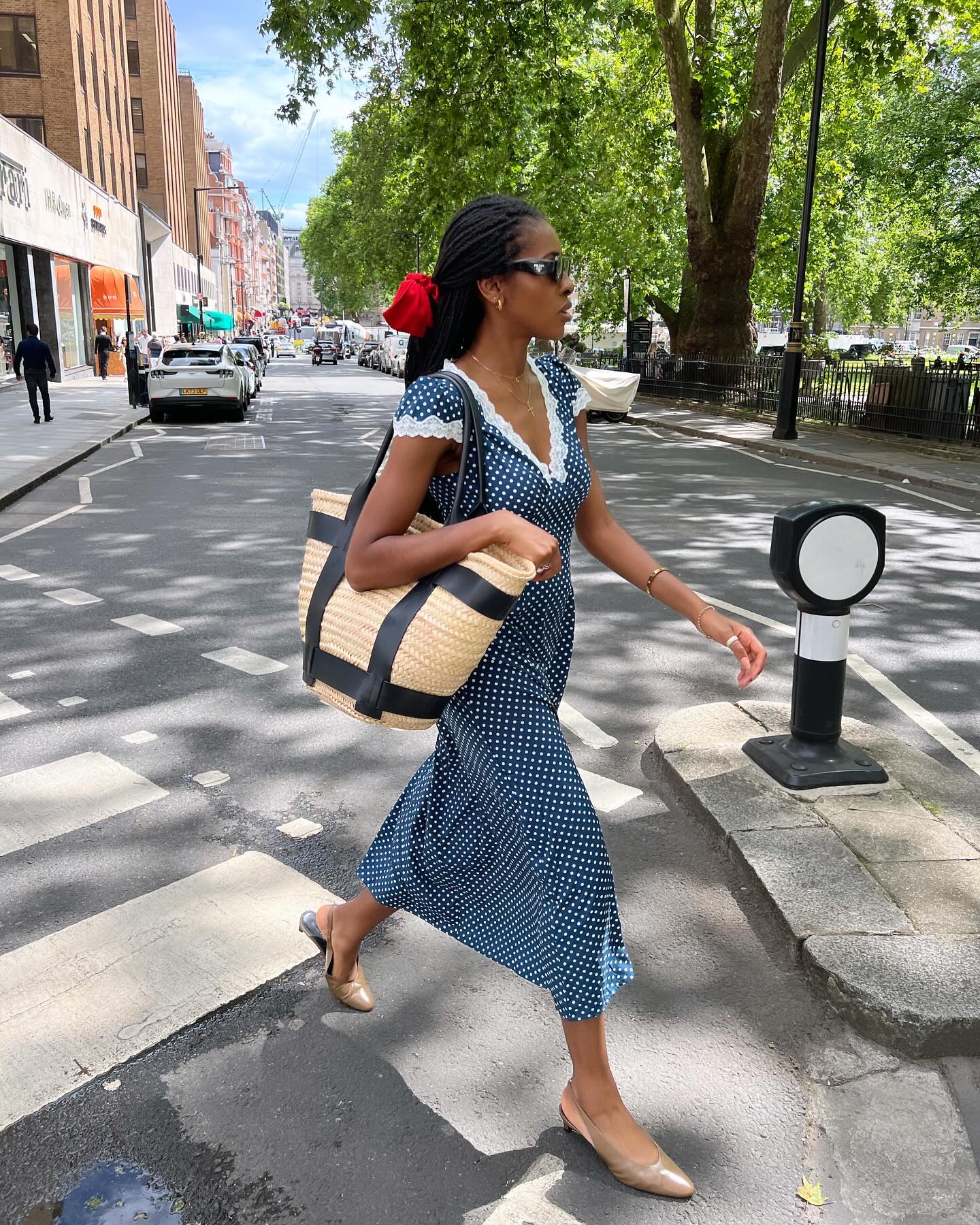 @georgia_3.0 wears a blue polka dot tea dress and a red scrunchie whilst crossing the road in London