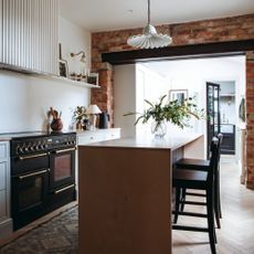 White painted kitchen with exposed brick feature wall, tall countertop, oven, and kitchen shelving
