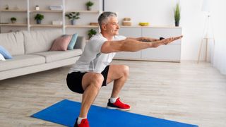 older man doing squats on a mat