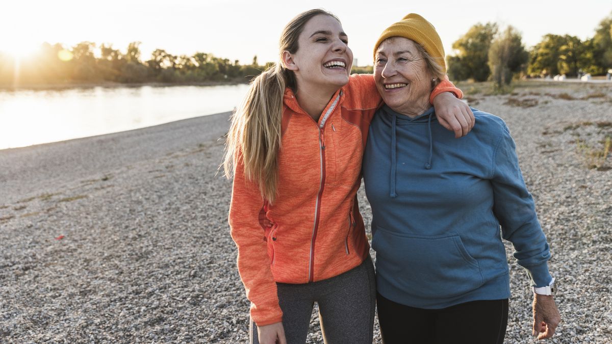 A young woman with blonde hair laughs and walks near a lake with her grandmother