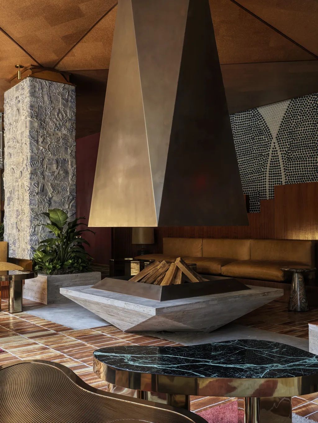 A glamorous, 1970s-inspired New York hotel boasts rooms defined by sleek, shiny surfaces, an earthy color palette, sculptural chandeliers and artwork accents, and textural details.