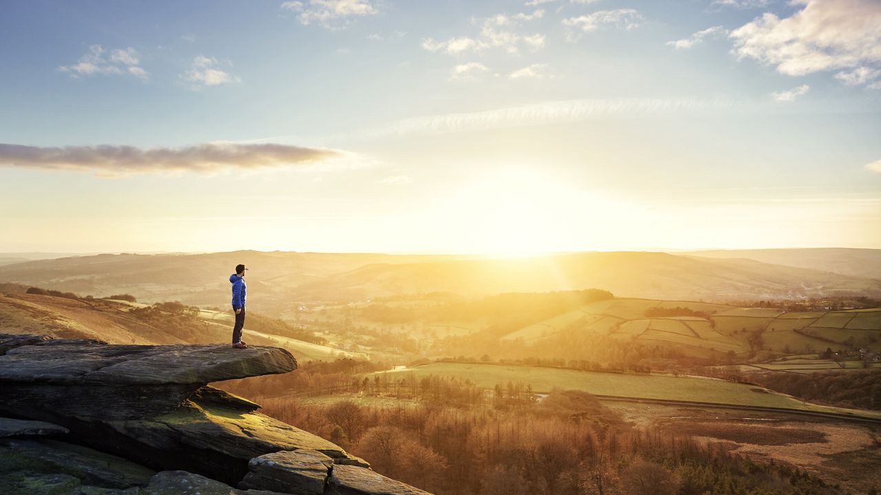 A hiker stands on a mountain watching the sun set.